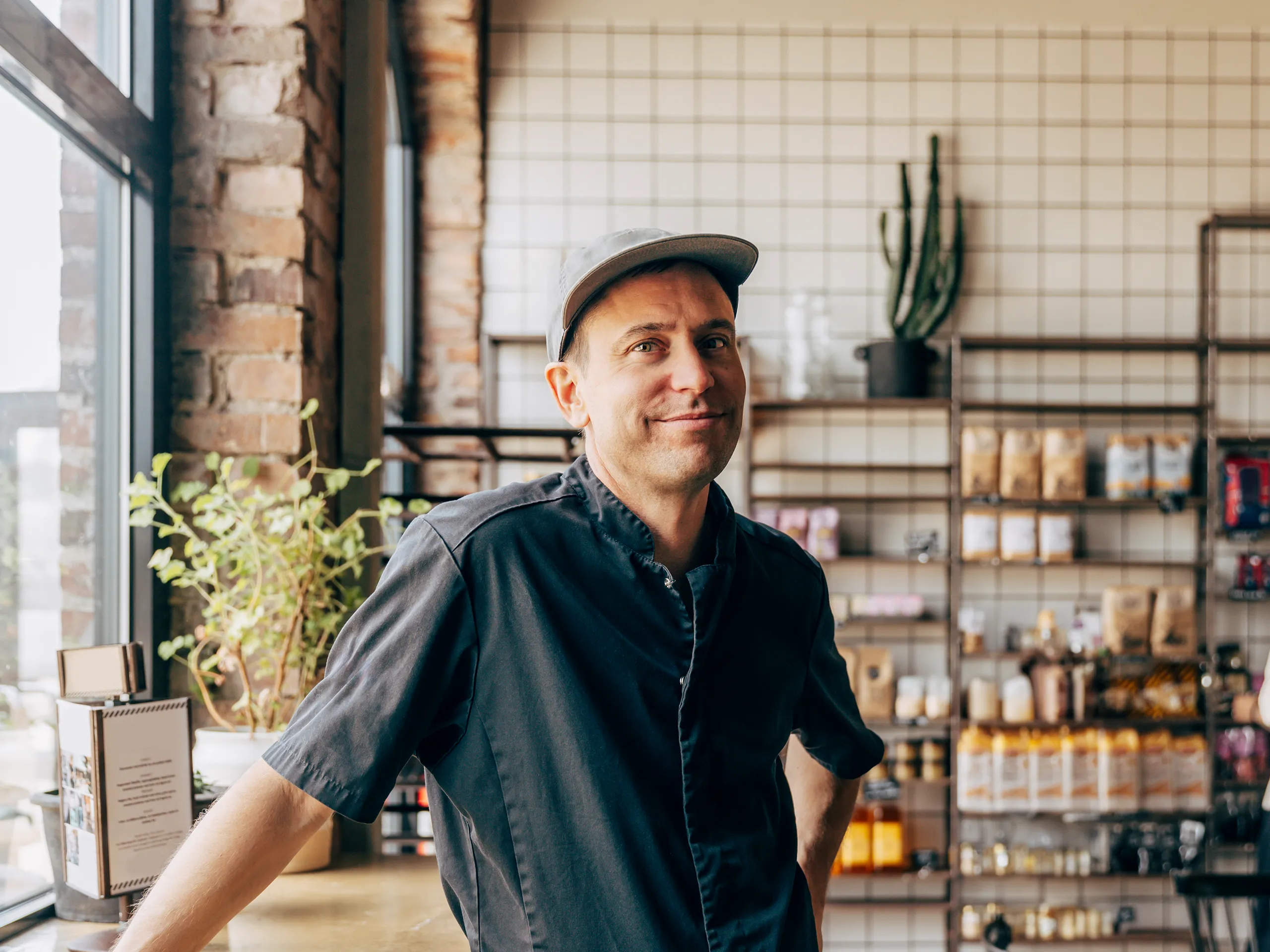 Café owner smiles in front of shelves with ingredients in a modern café.