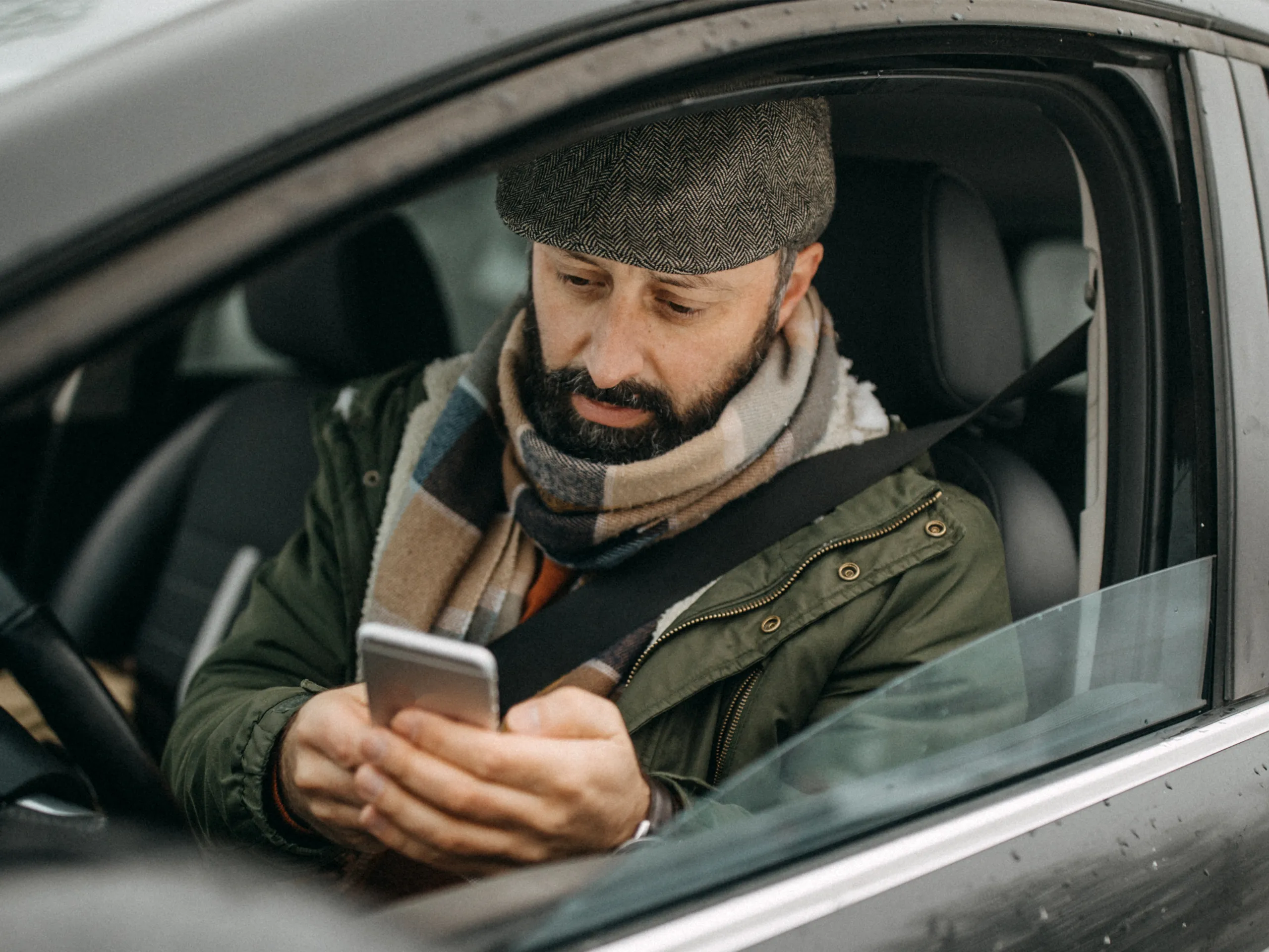 Man in a car types on his smartphone while wearing his seat belt.