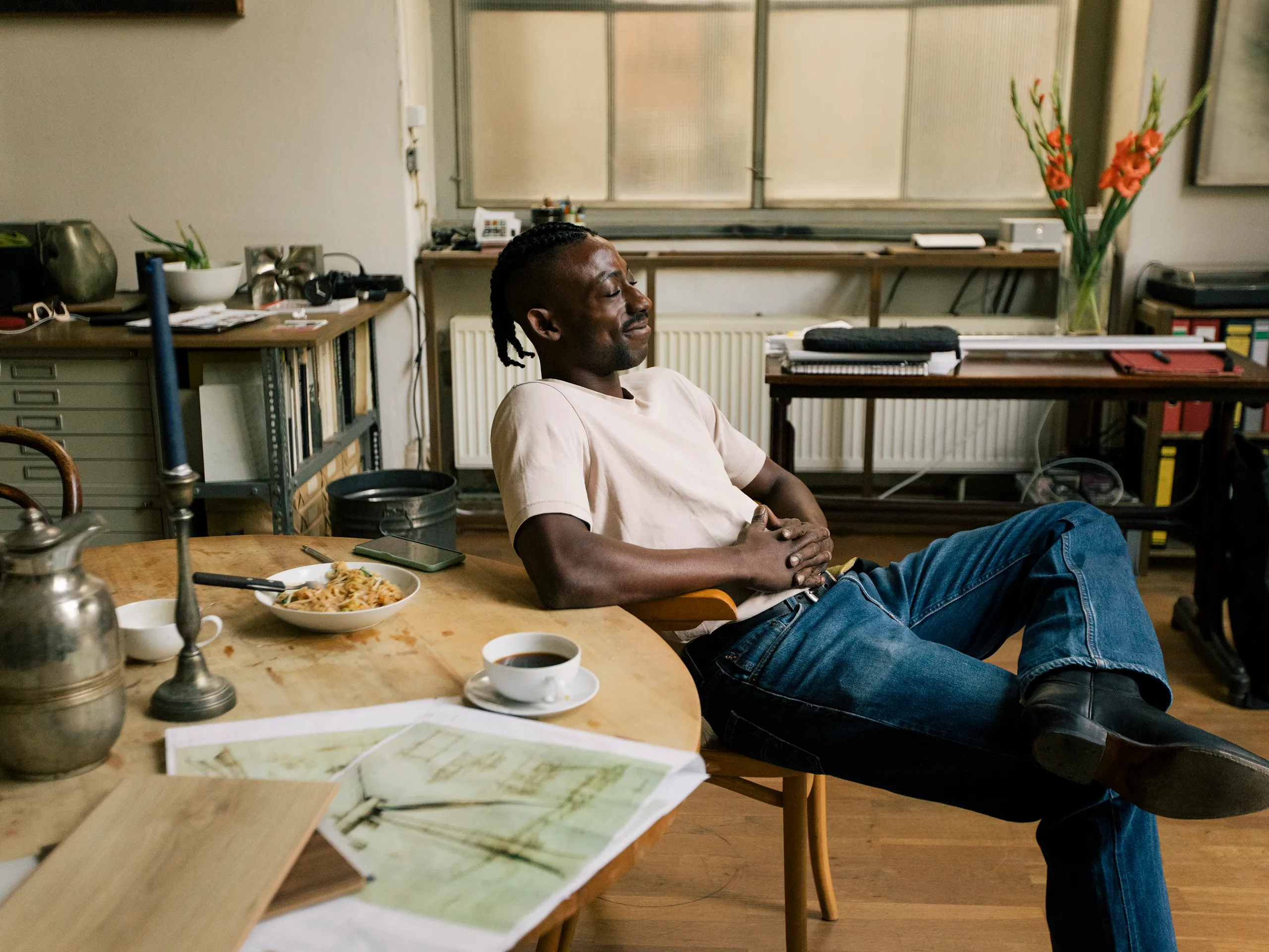 Man sits relaxed at a table with a cup of coffee and some food.