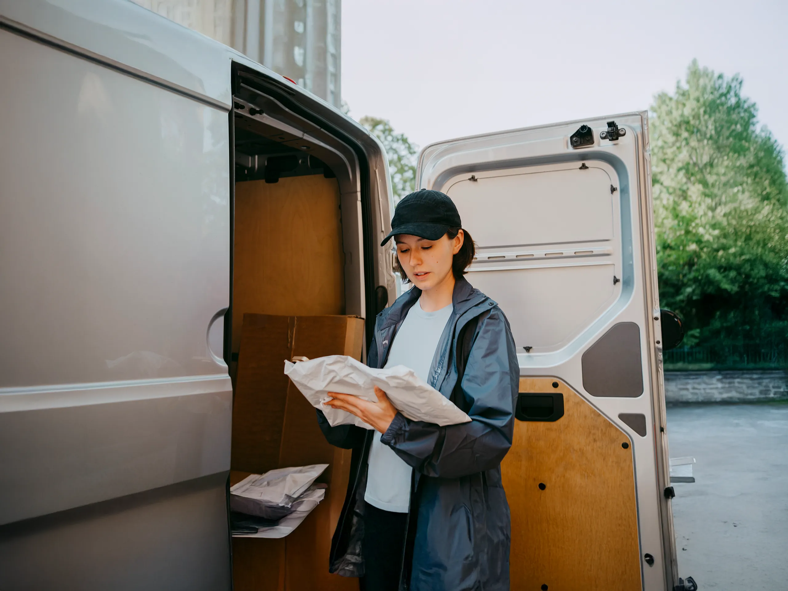 Parcel delivery woman checking a shipment in front of a delivery van.