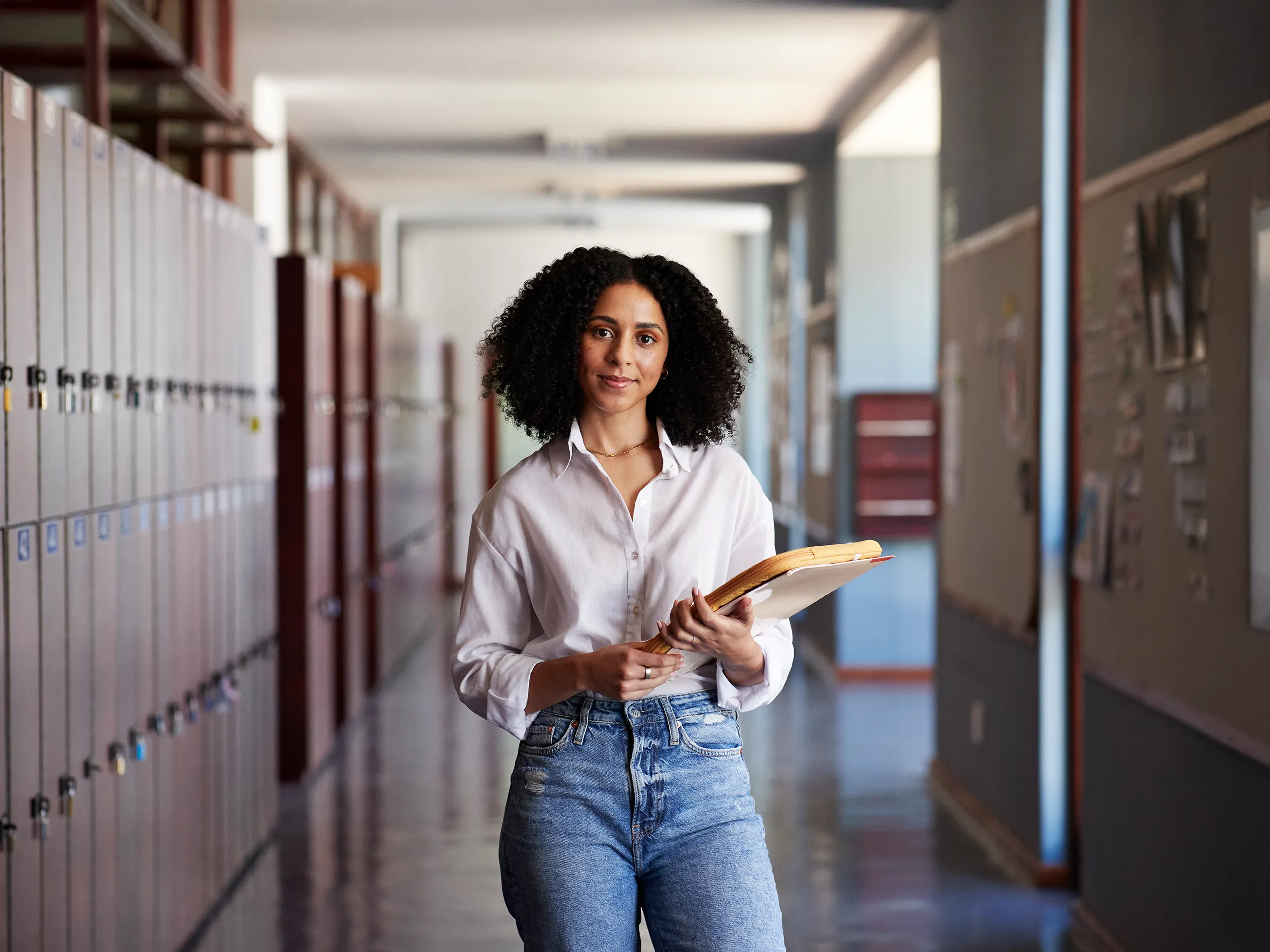 Teacher holding binders in a school hallway.