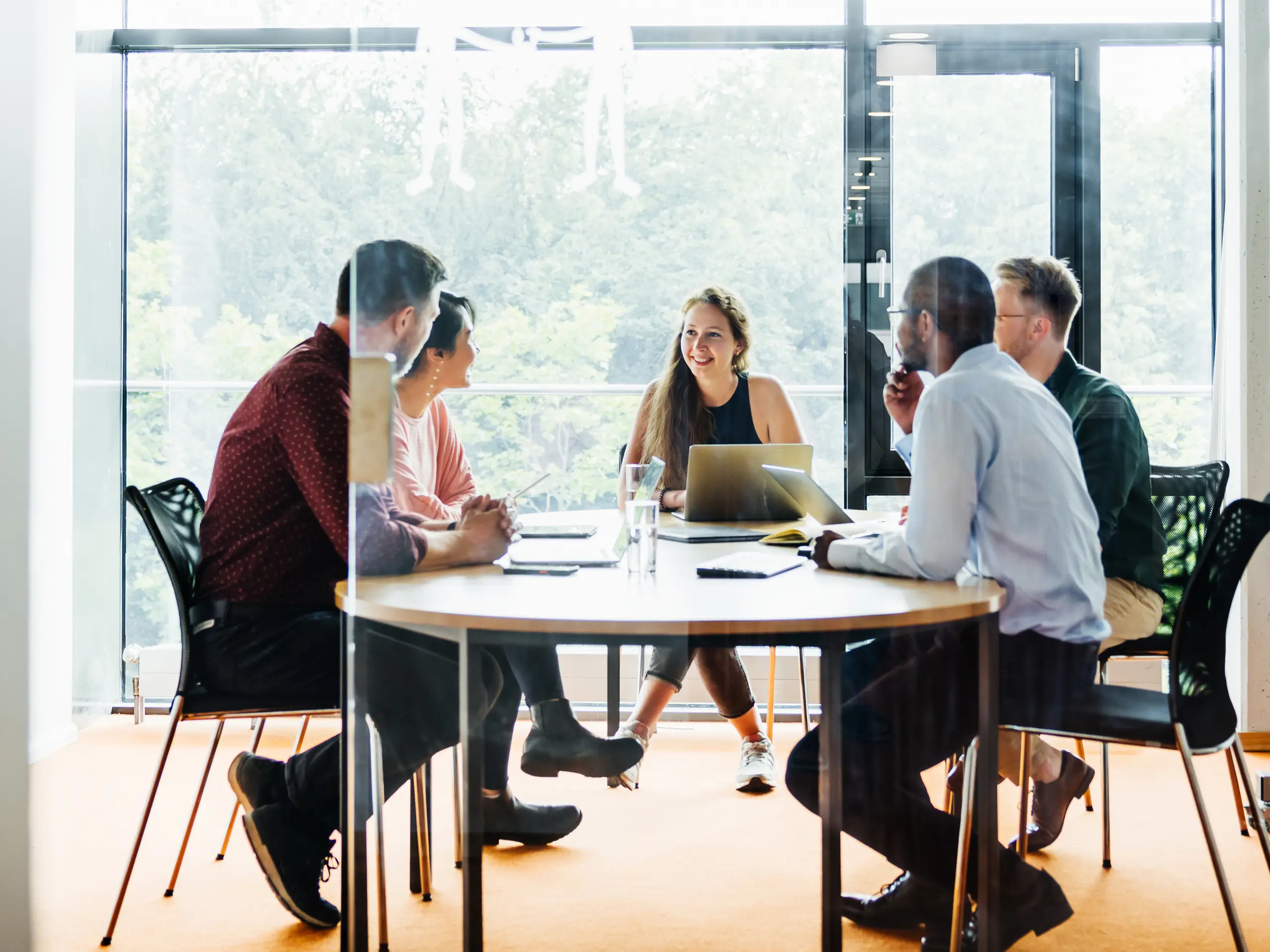 Several people sit around a meeting table in a modern conference room discussing projects, strategy, and collaboration.