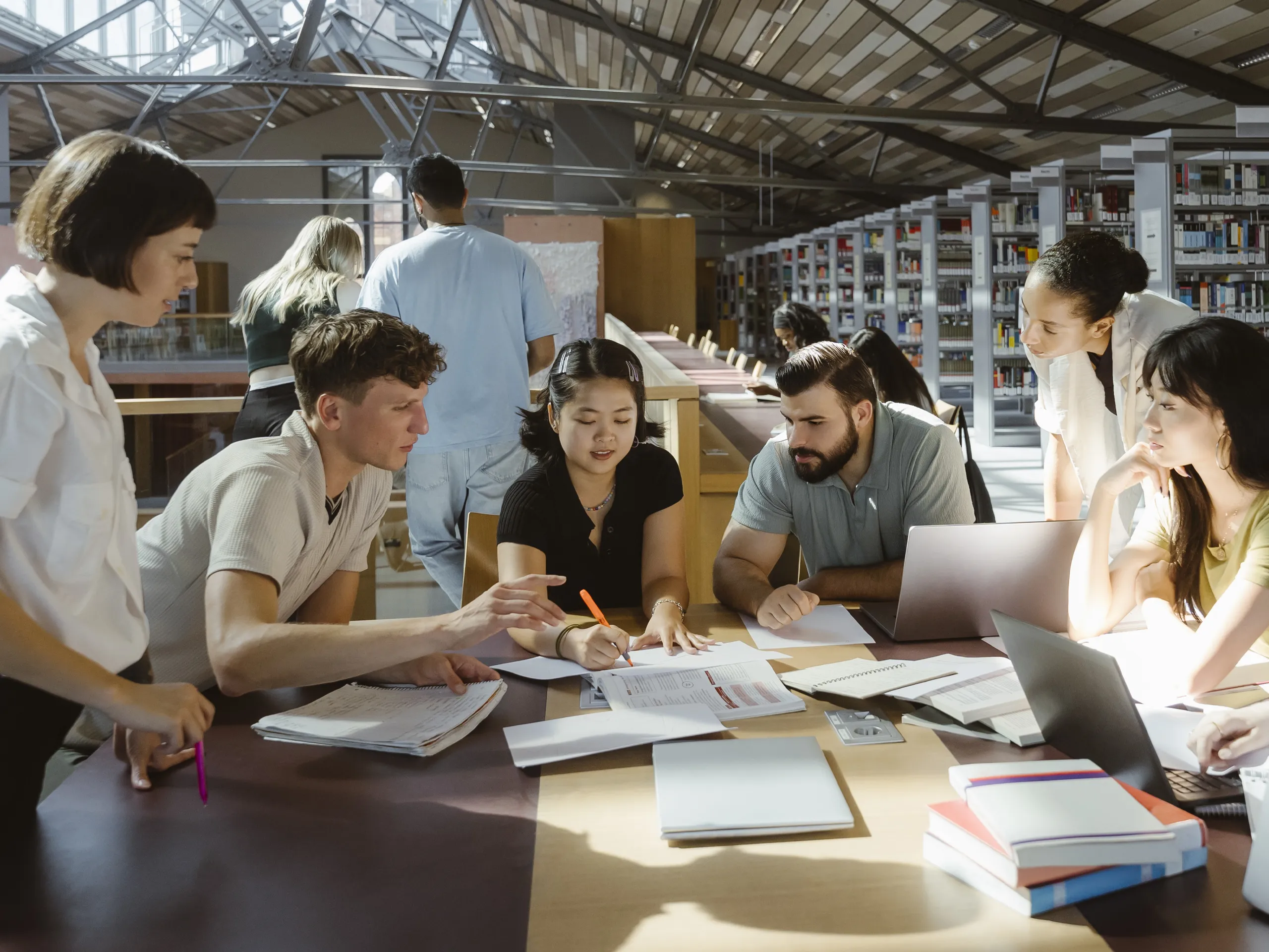Group of young people working together on documents in a library.