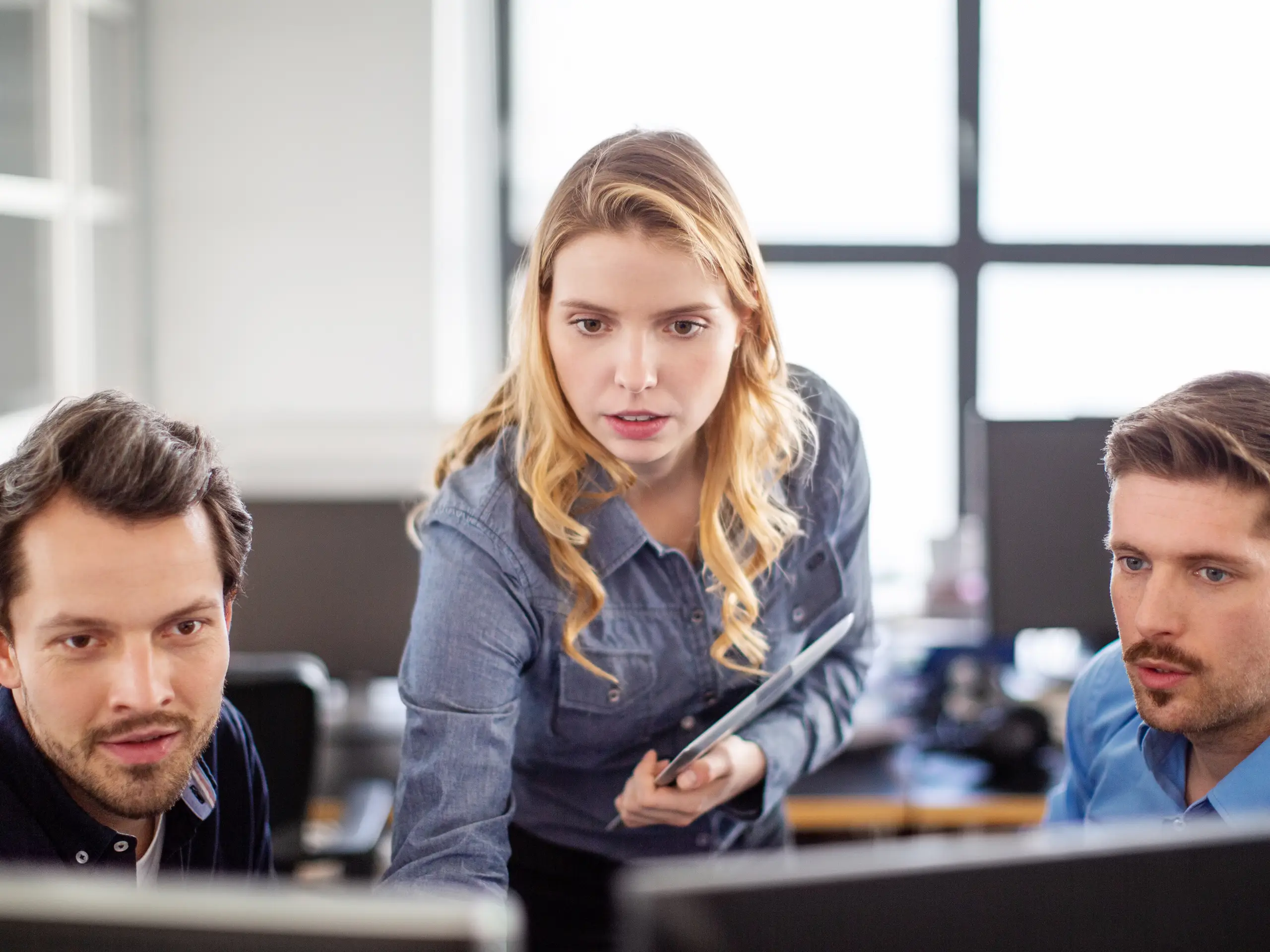 Three people looking at screens together, one person holding a tablet.