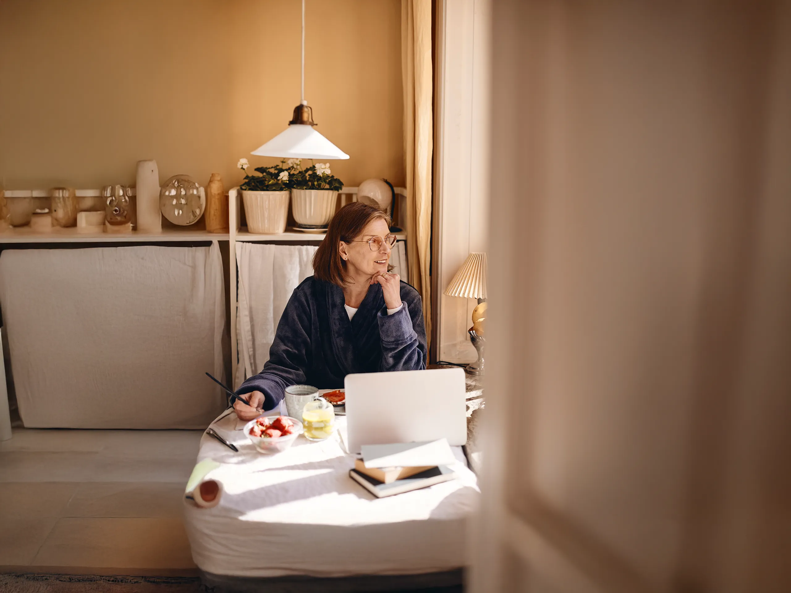 Woman having breakfast in a bathrobe and working on a laptop at home.