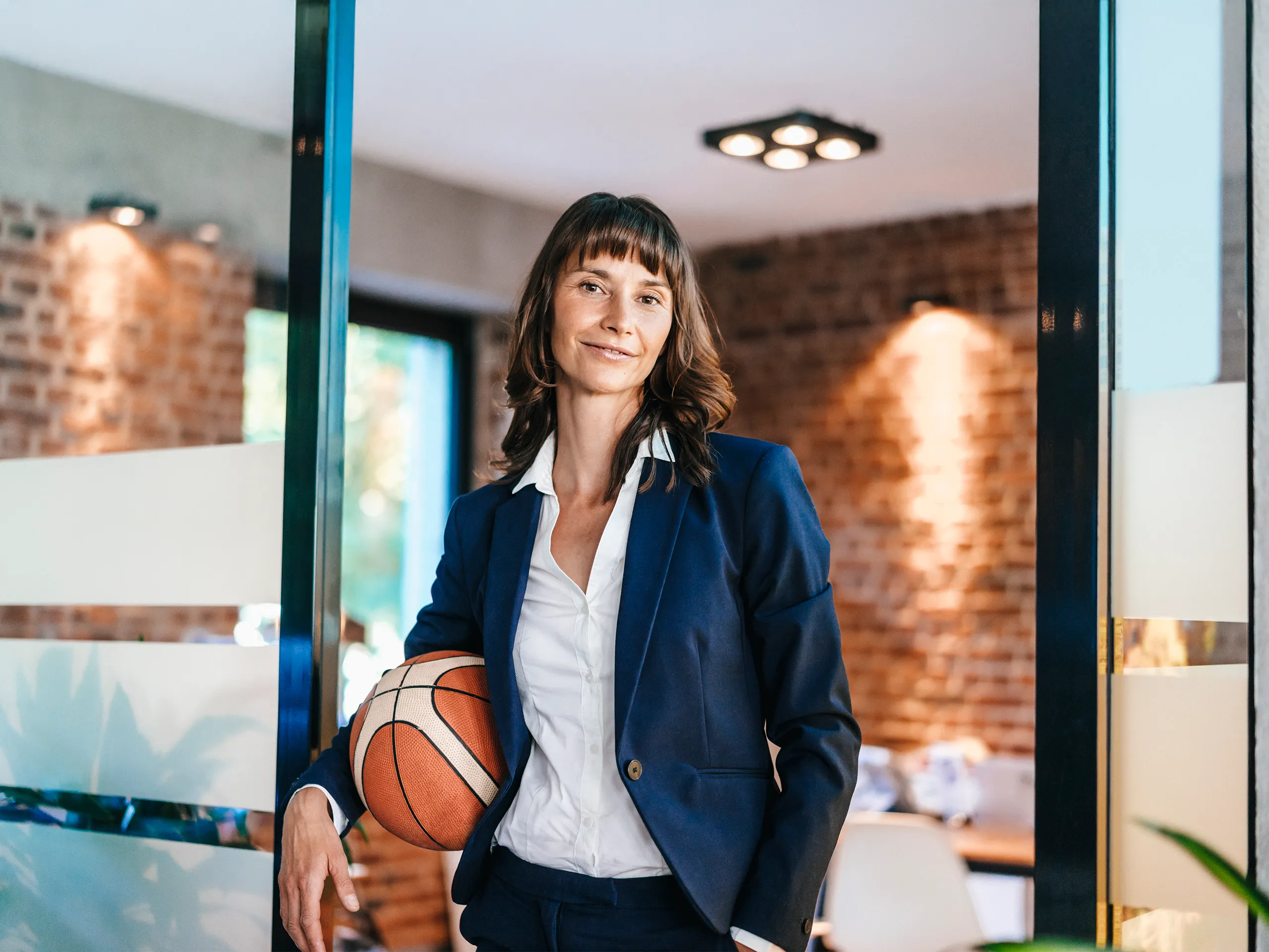 Smiling businesswoman in a suit holding a basketball in an office.
