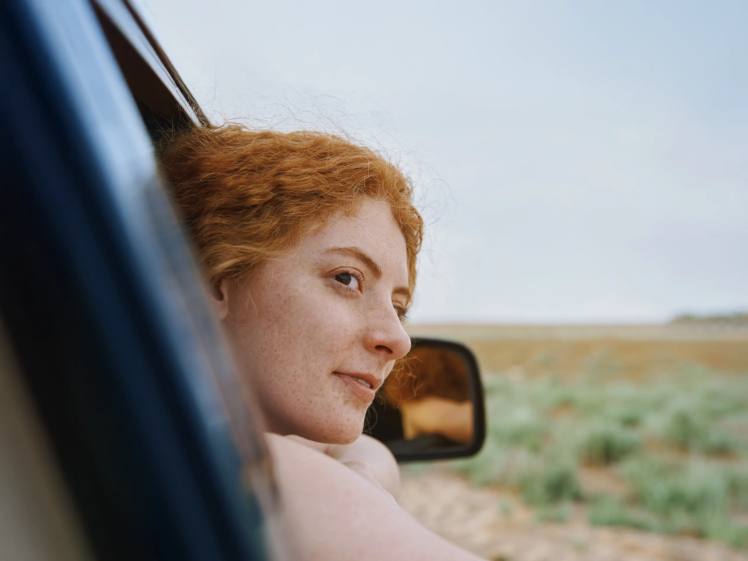 Woman with red hair leaning out of a car window.