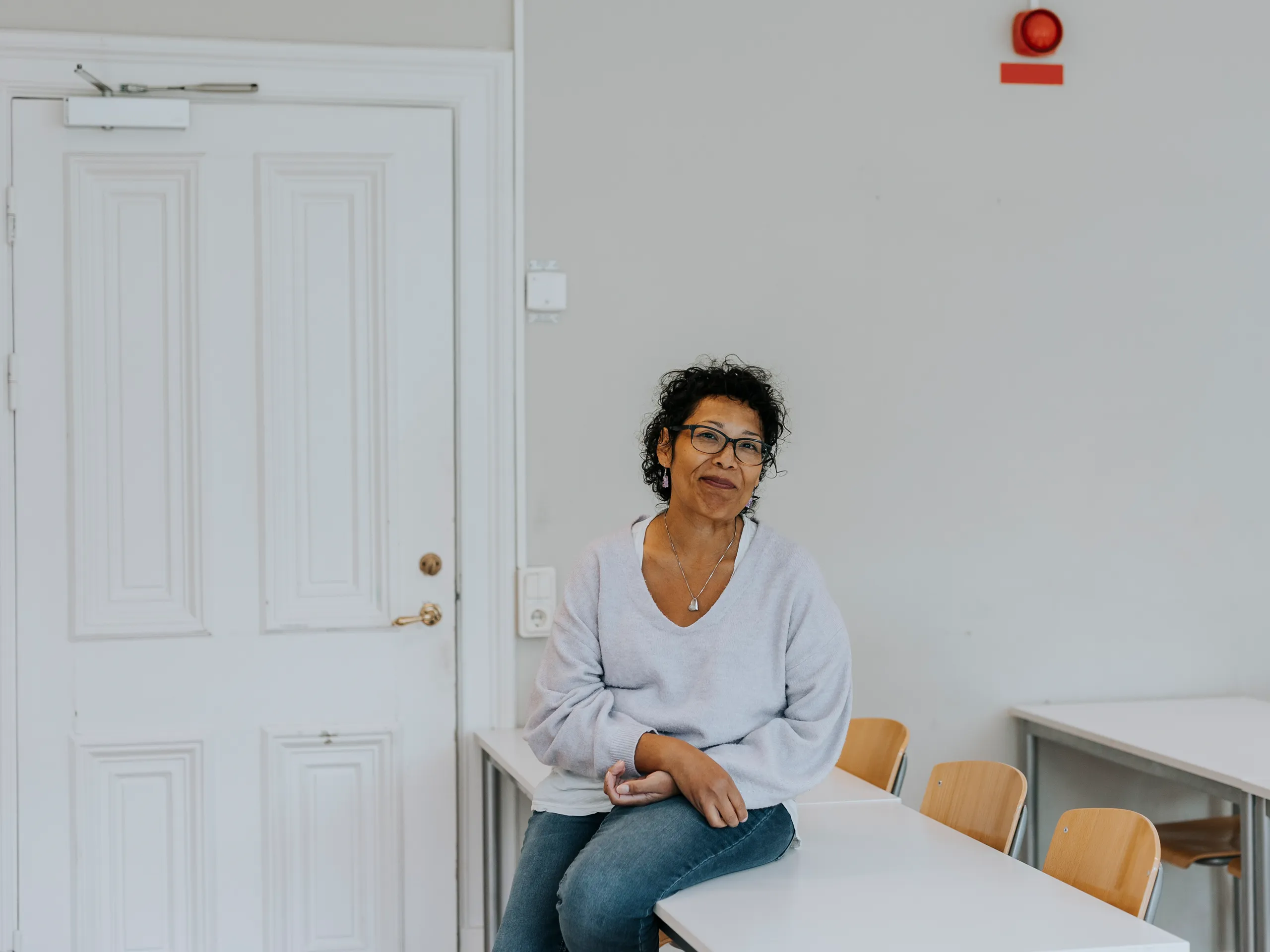 Relaxed woman with glasses sitting on a white table in a classroom.