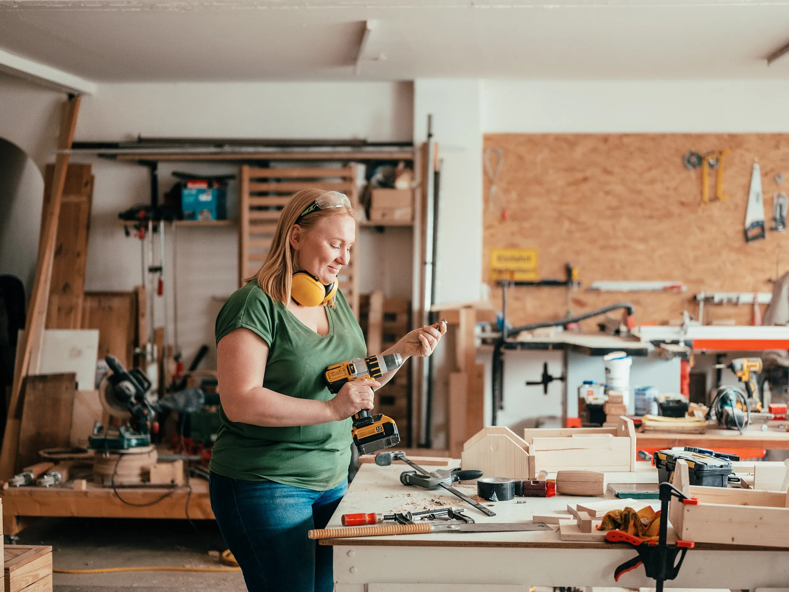 Woman working with focus using a drill in a well-equipped wood workshop.